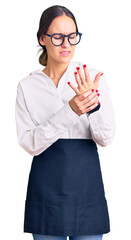 Beautiful brunette young woman wearing professional waitress apron suffering pain on hands and fingers, arthritis inflammation