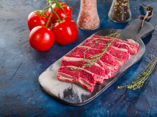 On a dark blue marble background, raw steaks from selected meat, pork fillet, veal and a sprig of rosemary, ripe tomatoes, spices and seasonings in glass jars. Cooking meat dishes, home cooking.