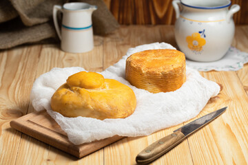 homemade wheel of cheese and pitcher of milk on wooden table.