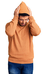 Fototapeta premium Handsome latin american young man wearing winter sweater and wool hat suffering from headache desperate and stressed because pain and migraine. hands on head.