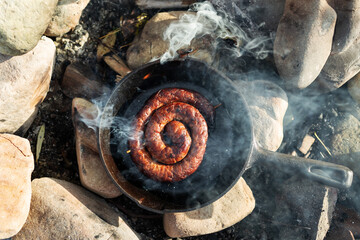 Sausage on the pan over an open fire. Preparing food in nature.