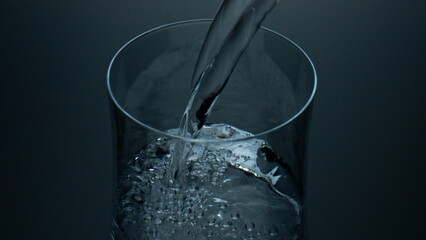 Pure water pouring cup closeup. Refreshing liquid bubbling filling glass jug