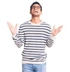 Hispanic handsome young man wearing casual clothes and glasses crazy and mad shouting and yelling with aggressive expression and arms raised. frustration concept.