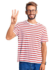 Naklejka premium Handsome blond man with beard wearing casual clothes and glasses showing and pointing up with fingers number three while smiling confident and happy.