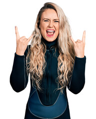 Young blonde woman wearing diver neoprene uniform shouting with crazy expression doing rock symbol...