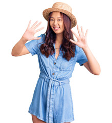 Obraz na płótnie Canvas Young beautiful chinese girl wearing summer hat showing and pointing up with fingers number ten while smiling confident and happy.
