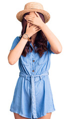 Fototapeta premium Young beautiful chinese girl wearing summer hat covering eyes and mouth with hands, surprised and shocked. hiding emotion