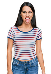 Young hispanic girl wearing casual striped t shirt sticking tongue out happy with funny expression. emotion concept.