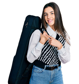Young brunette teenager wearing guitar case smiling happy pointing with hand and finger