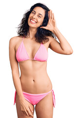 Young beautiful hispanic woman wearing bikini waiving saying hello happy and smiling, friendly welcome gesture