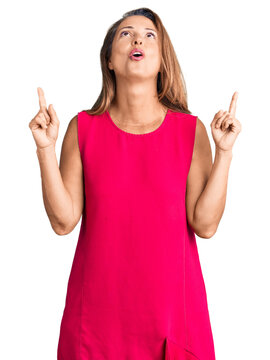 Middle age hispanic woman wearing casual clothes amazed and surprised looking up and pointing with fingers and raised arms.