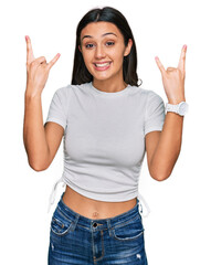 Young hispanic girl wearing casual white t shirt shouting with crazy expression doing rock symbol with hands up. music star. heavy music concept.