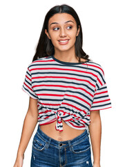 Fototapeta premium Young hispanic girl wearing casual clothes looking away to side with smile on face, natural expression. laughing confident.