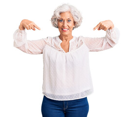 Senior grey-haired woman wearing casual clothes looking confident with smile on face, pointing...