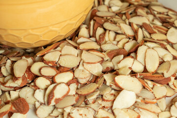A pile of slivered almonds next to a yellow bowl with honeycomb pattern.