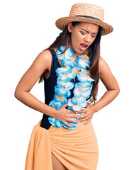 Young beautiful latin girl wearing hawaiian lei and summer hat with hand on stomach because nausea,...