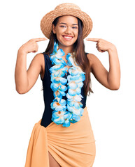 Young beautiful latin girl wearing hawaiian lei and summer hat smiling cheerful showing and...