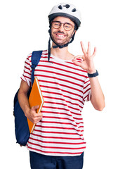 Young hispanic man wearing student backpack and bike helmet holding binder doing ok sign with fingers, smiling friendly gesturing excellent symbol
