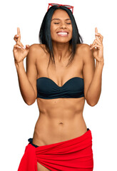 Young african american woman wearing bikini gesturing finger crossed smiling with hope and eyes closed. luck and superstitious concept.