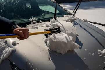 man cleaning snow off his car during winter snowfall. Sunny winter day 