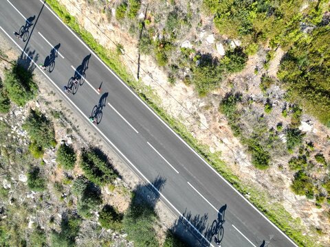 Aerial Top View Of Cyclists And Their Shadows On An Asphalt Road Through Mountains In Lisbon