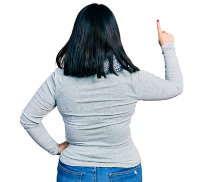 Young hispanic plus size woman wearing winter scarf posing backwards pointing ahead with finger hand