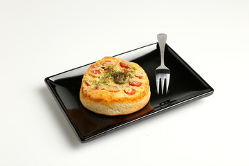 Open small pies, mini pizzas with sausage, pickles, tomatoes, mozzarella, mushroom, fork on a black square plate on a white background