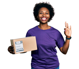 African american woman with afro hair holding delivery package doing ok sign with fingers, smiling...