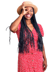 Young african american woman wearing summer hat doing ok gesture with hand smiling, eye looking through fingers with happy face.