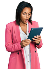 Beautiful hispanic woman using touchpad device scared and amazed with open mouth for surprise, disbelief face