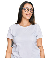 Young hispanic woman wearing casual white t shirt looking away to side with smile on face, natural expression. laughing confident.