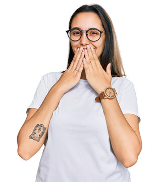 Young hispanic woman wearing casual white t shirt laughing and embarrassed giggle covering mouth with hands, gossip and scandal concept