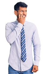 Young latin man wearing business clothes looking stressed and nervous with hands on mouth biting nails. anxiety problem.