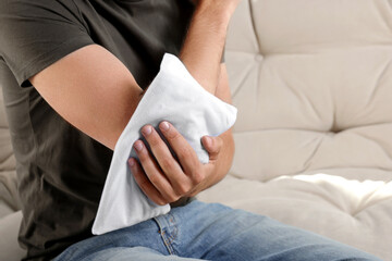 Man using heating pad on sofa, closeup. Space for text © New Africa