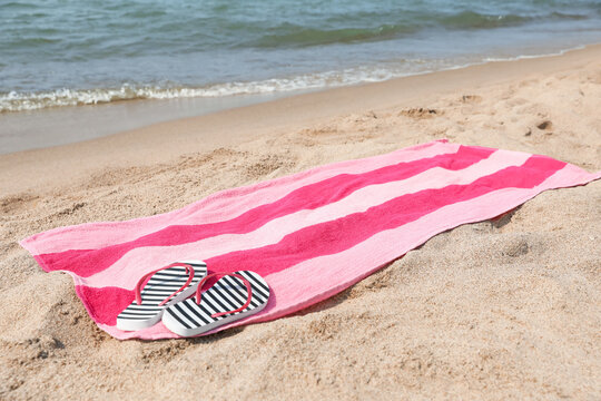 Pink striped towel with flip flops on beach sand near sea