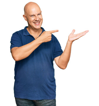 Middle age bald man wearing casual clothes amazed and smiling to the camera while presenting with hand and pointing with finger.