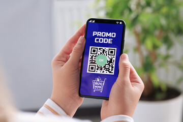 Woman holding smartphone with activated promo code in online shopping app indoors, closeup