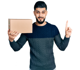 Young arab man with beard holding delivery package smiling with an idea or question pointing finger with happy face, number one