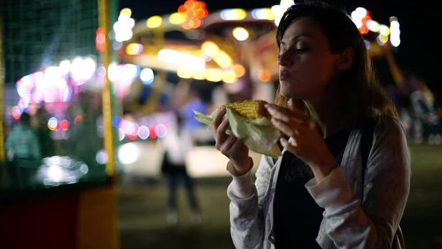 Young woman eating grilled corn at carnival