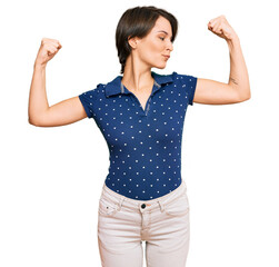 Young brunette woman with short hair wearing casual clothes showing arms muscles smiling proud. fitness concept.