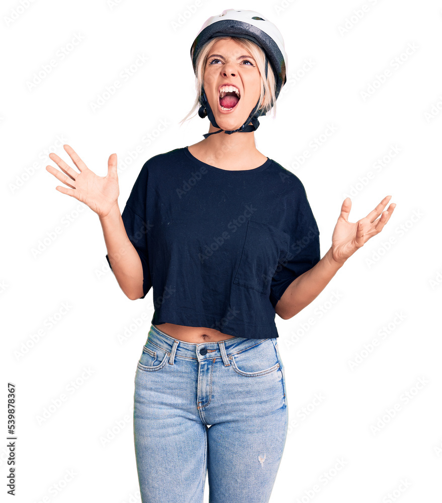 Poster Young beautiful blonde woman wearing bike helmet crazy and mad shouting and yelling with aggressive expression and arms raised. frustration concept.