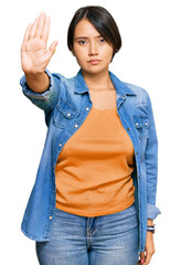 Young beautiful hispanic woman with short hair wearing casual denim jacket doing stop sing with palm of the hand. warning expression with negative and serious gesture on the face.