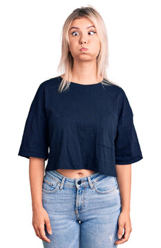 Young beautiful blonde woman wearing casual t-shirt puffing cheeks with funny face. mouth inflated with air, crazy expression.