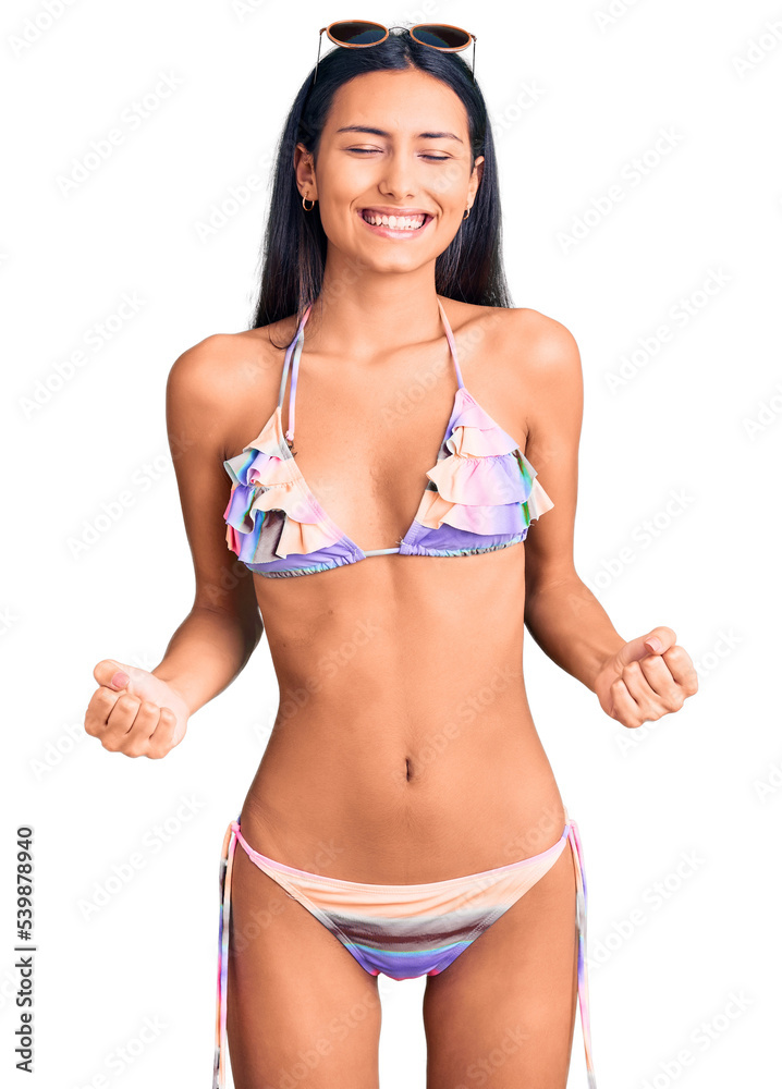 Sticker young beautiful latin girl wearing bikini and sunglasses very happy and excited doing winner gesture