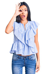 Fototapeta premium Young beautiful latin girl wearing casual clothes doing ok gesture shocked with surprised face, eye looking through fingers. unbelieving expression.