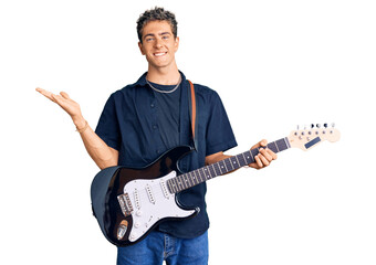 Obraz premium Young handsome man playing electric guitar celebrating victory with happy smile and winner expression with raised hands