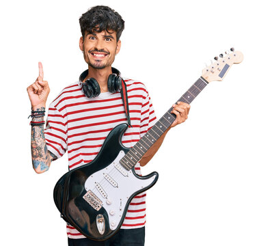 Young hispanic man playing electric guitar surprised with an idea or question pointing finger with happy face, number one