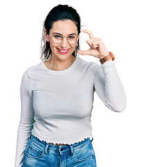 Young hispanic woman wearing casual clothes smiling and confident gesturing with hand doing small size sign with fingers looking and the camera. measure concept.