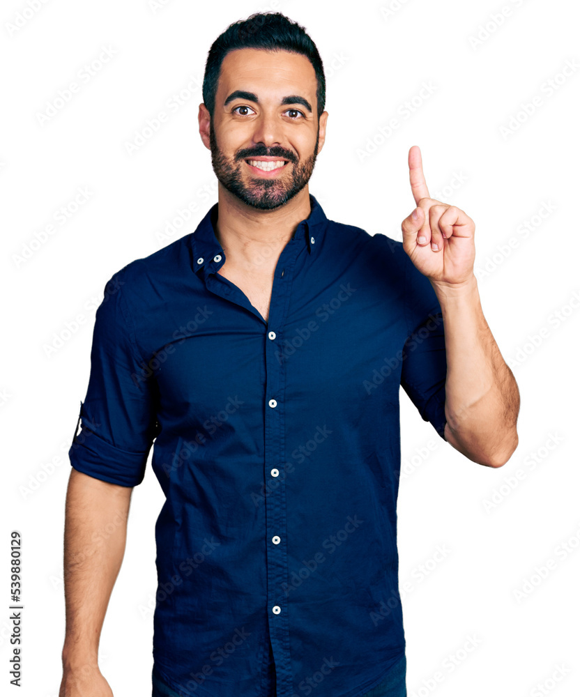 Sticker Young hispanic man with beard wearing casual blue shirt pointing finger up with successful idea. exited and happy. number one.