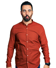 Young hispanic man with beard wearing casual shirt making fish face with lips, crazy and comical gesture. funny expression.